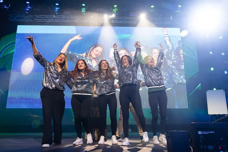 Cinco integrantes del equipo en el escenario con los brazos en alto ante una pantalla LED