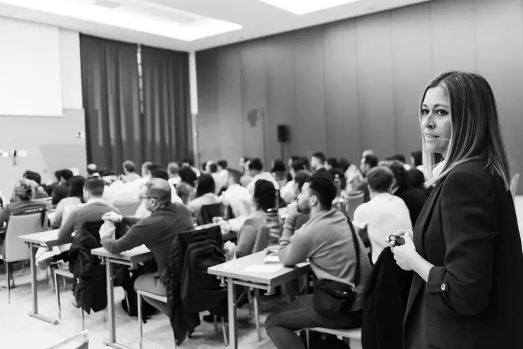 Sala de formación llena, con asistentes sentados en mesas siguiendo la ponencia